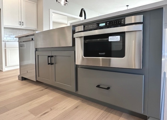 kitchen featuring light hardwood / wood-style floors, tasteful backsplash, appliances with stainless steel finishes, white cabinetry, and gray cabinetry