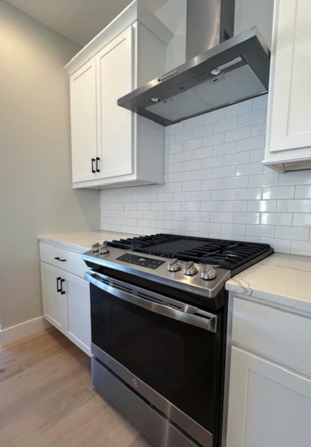 kitchen featuring backsplash, gas stove, light hardwood / wood-style floors, white cabinets, and wall chimney range hood