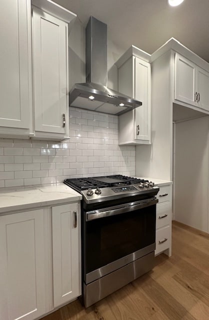 kitchen with white cabinetry, wall chimney range hood, stainless steel range with gas stovetop, and light hardwood / wood-style floors