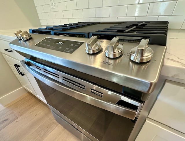 details featuring stainless steel gas stove, backsplash, and light hardwood / wood-style flooring