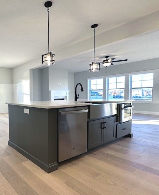 kitchen featuring decorative light fixtures, ceiling fan, appliances with stainless steel finishes, light hardwood / wood-style flooring, and a center island with sink