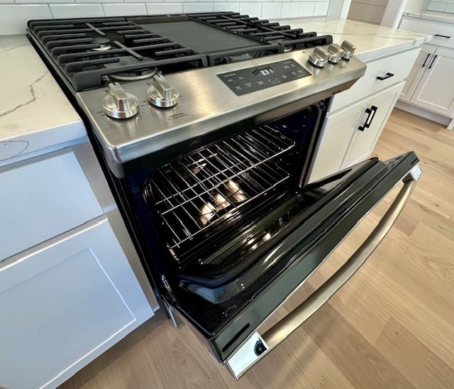 interior details featuring light wood-type flooring, tasteful backsplash, and stainless steel range with gas stovetop