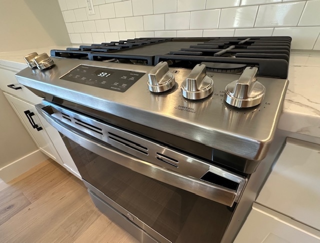 details with light hardwood / wood-style floors, backsplash, and gas range