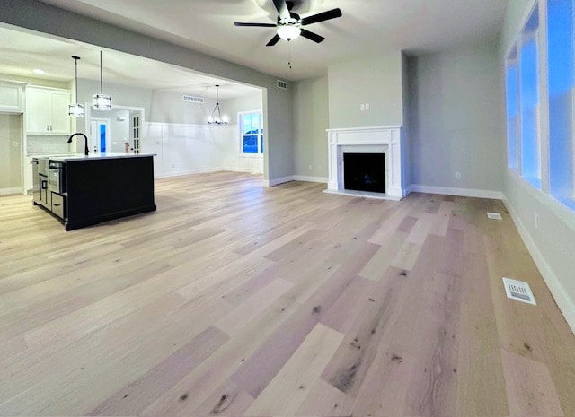 unfurnished living room featuring ceiling fan with notable chandelier, a wealth of natural light, and light wood-type flooring