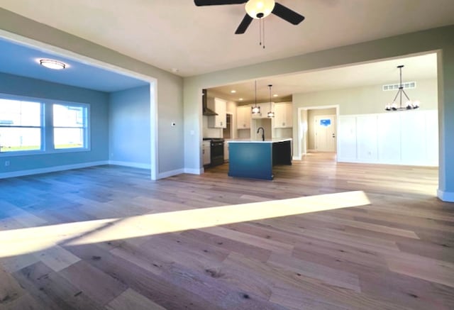 unfurnished living room featuring ceiling fan with notable chandelier, sink, and wood-type flooring