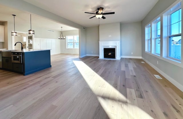 unfurnished living room with light hardwood / wood-style floors, sink, and ceiling fan with notable chandelier