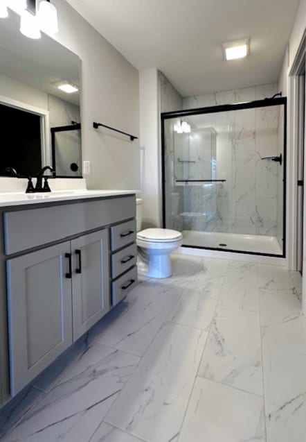 bathroom with a shower with shower door, vanity, toilet, and tile floors