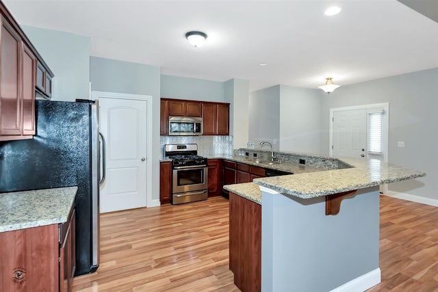 kitchen with stainless steel appliances, kitchen peninsula, light hardwood / wood-style flooring, light stone countertops, and backsplash