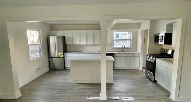 kitchen featuring appliances with stainless steel finishes, light wood-type flooring, white cabinets, a kitchen island, and tasteful backsplash