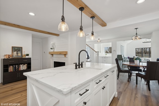 kitchen with pendant lighting, white cabinetry, beam ceiling, and a kitchen island with sink