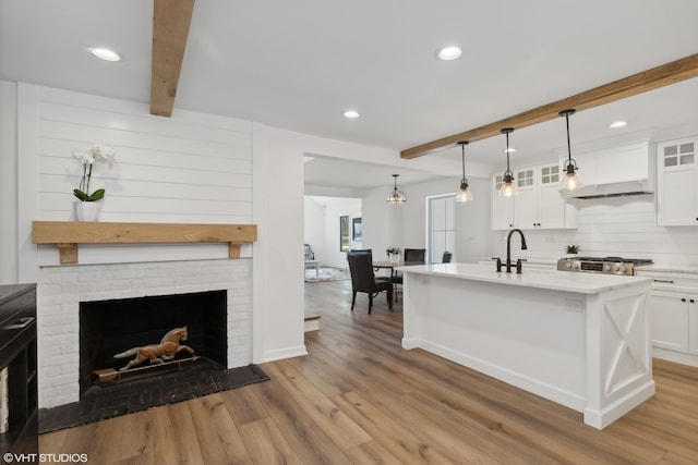 kitchen with light wood-type flooring, pendant lighting, a brick fireplace, beam ceiling, and white cabinets