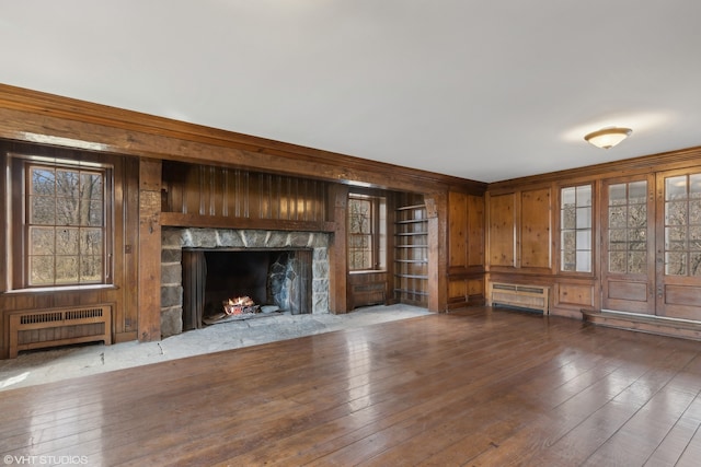 unfurnished living room featuring radiator heating unit, a wealth of natural light, wood-type flooring, and a stone fireplace