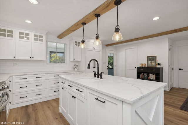 kitchen with hanging light fixtures, light hardwood / wood-style floors, white cabinetry, sink, and a center island with sink