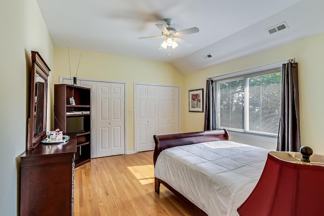 bedroom with two closets, ceiling fan, light hardwood / wood-style flooring, and vaulted ceiling