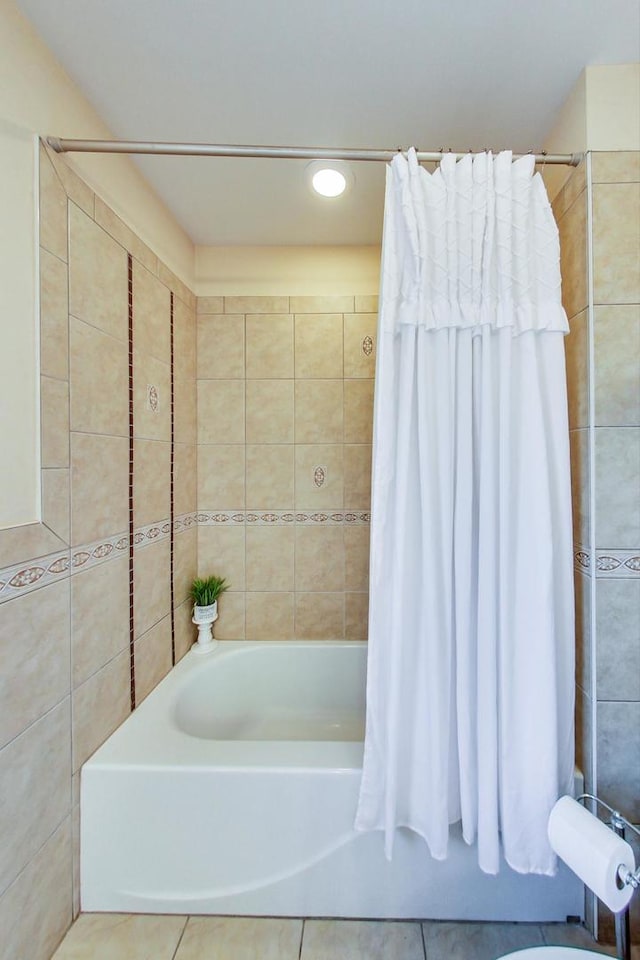 bathroom with tile walls, shower / bath combination with curtain, and tile patterned floors