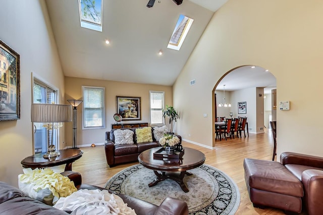 living room featuring high vaulted ceiling, a skylight, a notable chandelier, and light hardwood / wood-style flooring