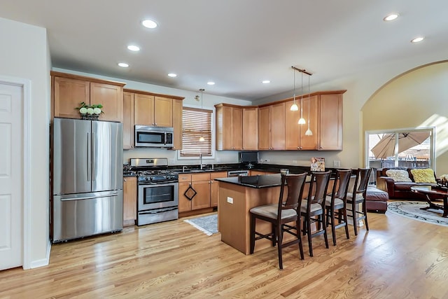 kitchen with stainless steel appliances, pendant lighting, sink, a kitchen breakfast bar, and light hardwood / wood-style floors