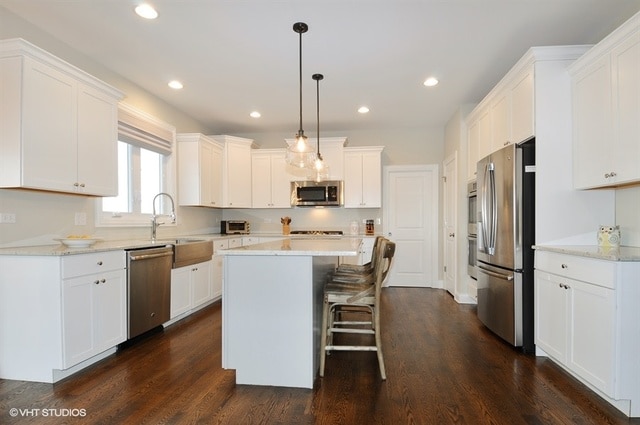 kitchen with decorative light fixtures, appliances with stainless steel finishes, a kitchen island, dark hardwood / wood-style floors, and white cabinetry