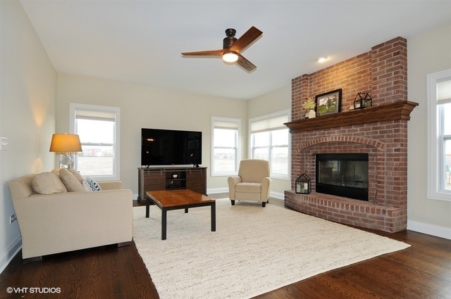 living room with a fireplace, dark wood-type flooring, brick wall, and plenty of natural light