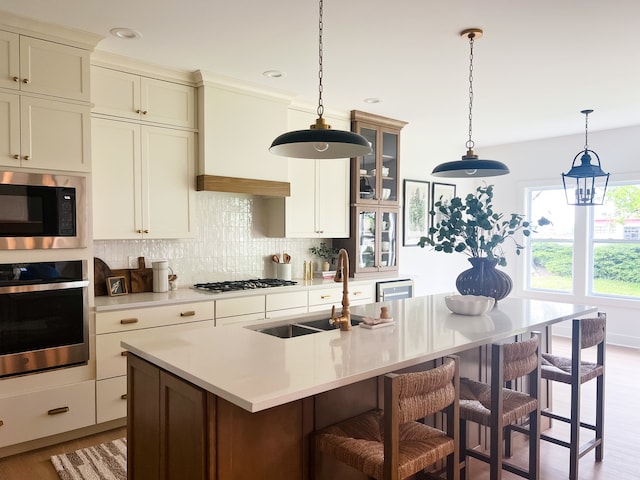 kitchen with appliances with stainless steel finishes, tasteful backsplash, an island with sink, light wood-type flooring, and sink