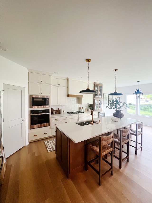 kitchen with light hardwood / wood-style floors, stainless steel appliances, white cabinetry, and a center island with sink