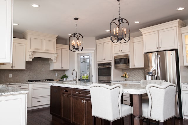 kitchen featuring decorative light fixtures, appliances with stainless steel finishes, light stone counters, a notable chandelier, and backsplash