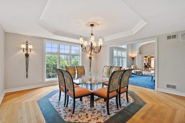 dining space featuring an inviting chandelier, a raised ceiling, and ornamental molding