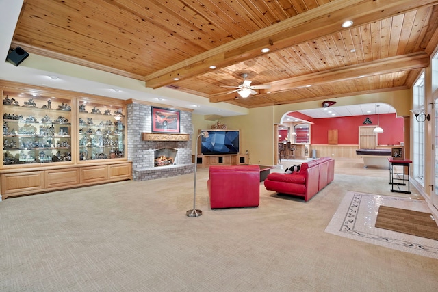 living room featuring beam ceiling, ceiling fan, a brick fireplace, brick wall, and carpet