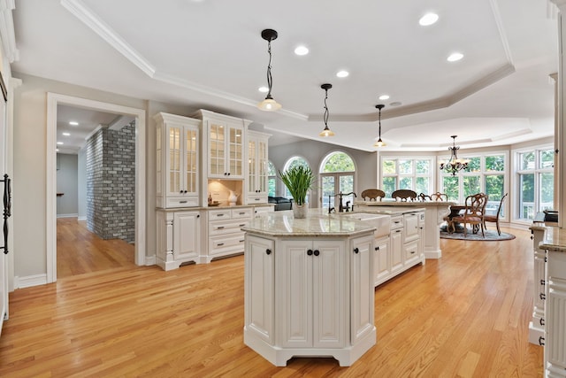 kitchen with light hardwood / wood-style flooring, a center island with sink, decorative light fixtures, white cabinetry, and a tray ceiling