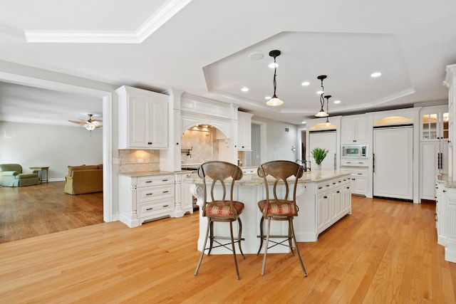 kitchen featuring built in appliances, light hardwood / wood-style flooring, white cabinets, a center island, and a raised ceiling