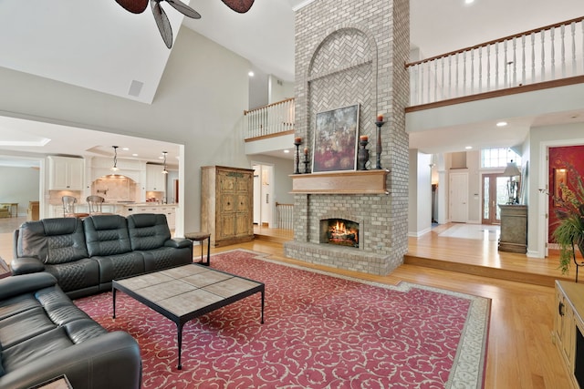 living room with a fireplace, hardwood / wood-style flooring, ceiling fan, high vaulted ceiling, and brick wall