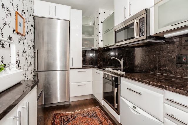 kitchen featuring dark stone countertops, decorative backsplash, white cabinetry, dark wood-type flooring, and appliances with stainless steel finishes