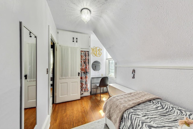 bedroom featuring lofted ceiling, light hardwood / wood-style flooring, and a textured ceiling