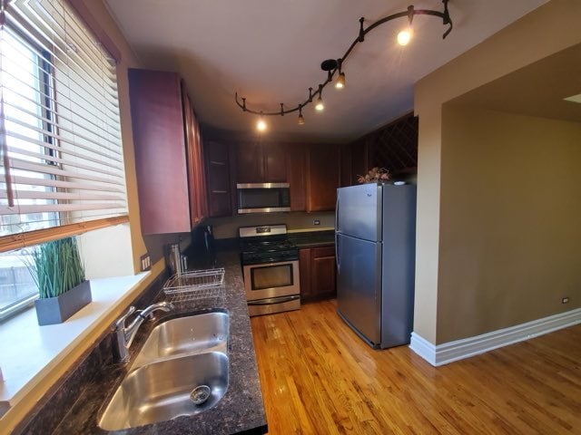 kitchen featuring dark stone counters, light hardwood / wood-style floors, rail lighting, stainless steel appliances, and sink