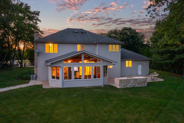 back house at dusk with a patio, a lawn, and central AC