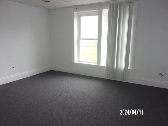 empty room featuring dark colored carpet, a healthy amount of sunlight, and a drop ceiling