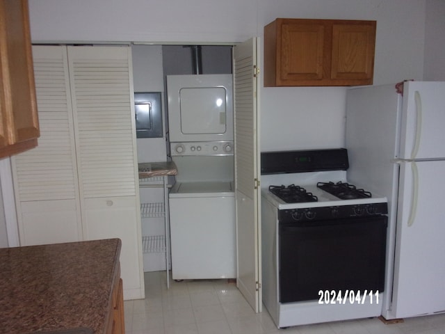 kitchen with white appliances, light tile floors, and stacked washing maching and dryer