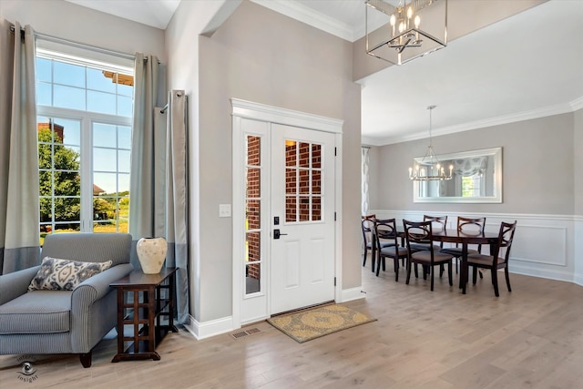 entrance foyer with ornamental molding, light hardwood / wood-style flooring, and a notable chandelier