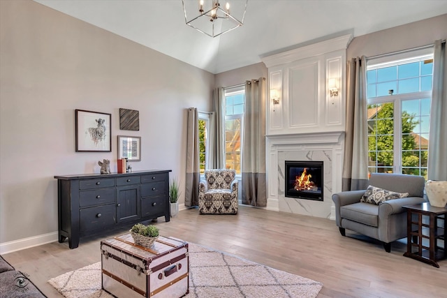 living room featuring an inviting chandelier, a premium fireplace, light hardwood / wood-style flooring, and high vaulted ceiling