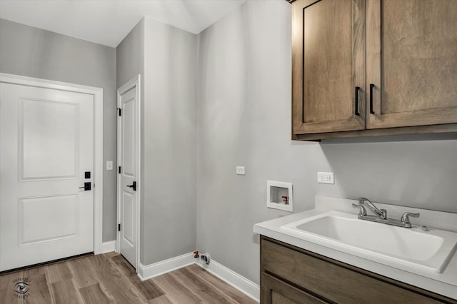 clothes washing area with light hardwood / wood-style flooring, sink, washer hookup, and cabinets