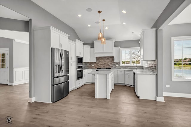 kitchen with appliances with stainless steel finishes, a center island, backsplash, light wood-type flooring, and lofted ceiling