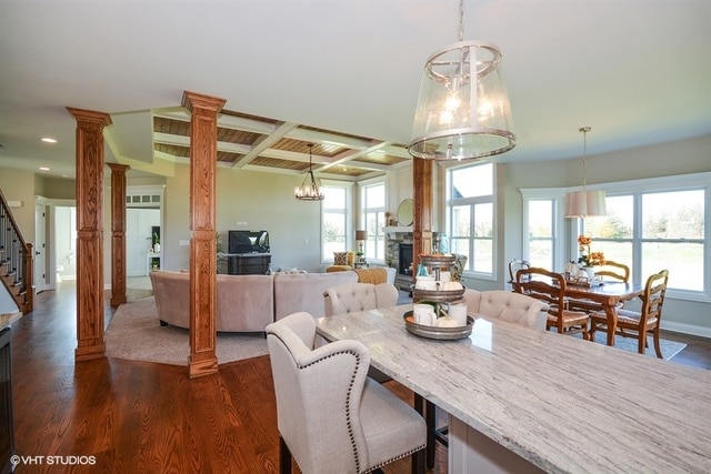 dining room with beamed ceiling, a stone fireplace, coffered ceiling, dark hardwood / wood-style flooring, and decorative columns