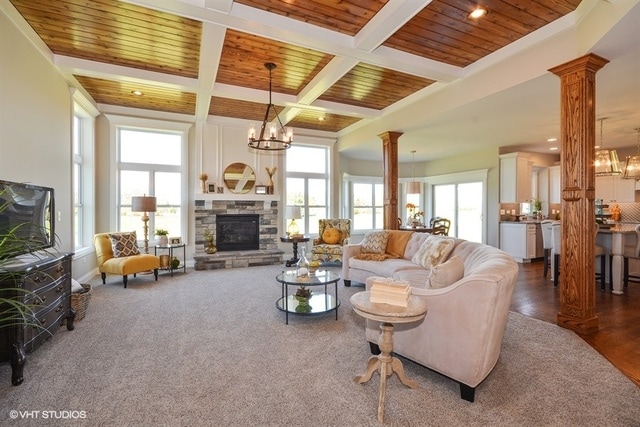 living room with ornate columns, a wealth of natural light, coffered ceiling, and an inviting chandelier