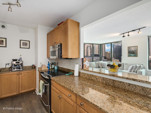 kitchen with appliances with stainless steel finishes, dark wood-type flooring, rail lighting, and light stone countertops