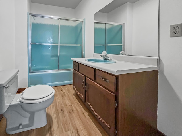 full bathroom with vanity with extensive cabinet space, wood-type flooring, toilet, and bath / shower combo with glass door