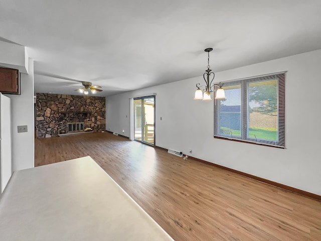 interior space with ceiling fan with notable chandelier, a stone fireplace, and wood-type flooring