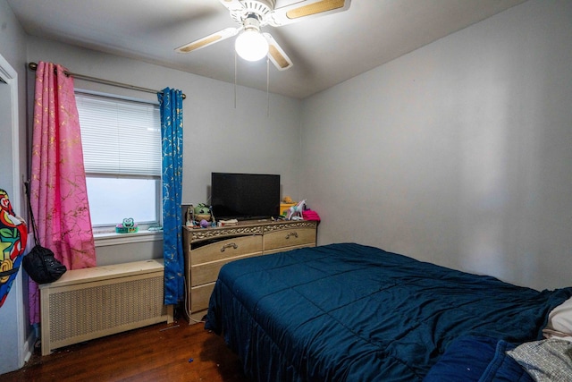 bedroom featuring dark hardwood / wood-style flooring, ceiling fan, and radiator heating unit