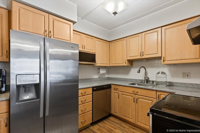 kitchen featuring stainless steel appliances, wood-type flooring, tasteful backsplash, light stone counters, and sink