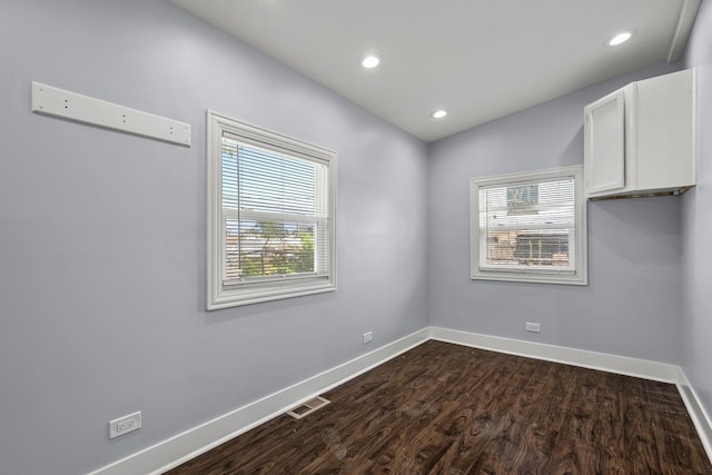 empty room featuring dark wood-style flooring, a healthy amount of sunlight, visible vents, and baseboards