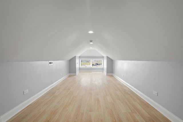 additional living space with light wood-style floors, baseboards, visible vents, and vaulted ceiling